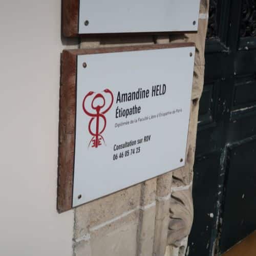 Plaque professionnelle d'Amandine Held, étiopathe à Paris 4, indiquant les coordonnées pour prendre rendez-vous.